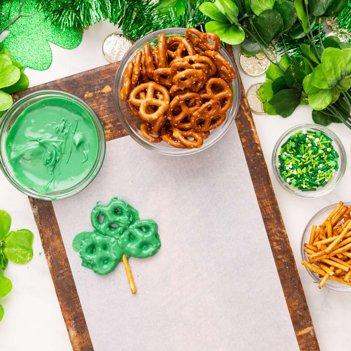 three pretzels covered in green chocolate and a pretzel stick made to look like a shamrock drying on parchment paper.
