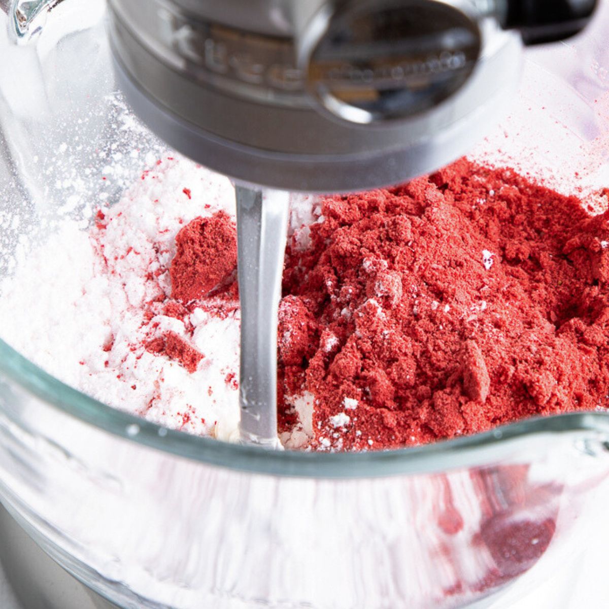powdered sugar and freeze dried strawberries on top of creamed butter in the bowl of a standing mixer.