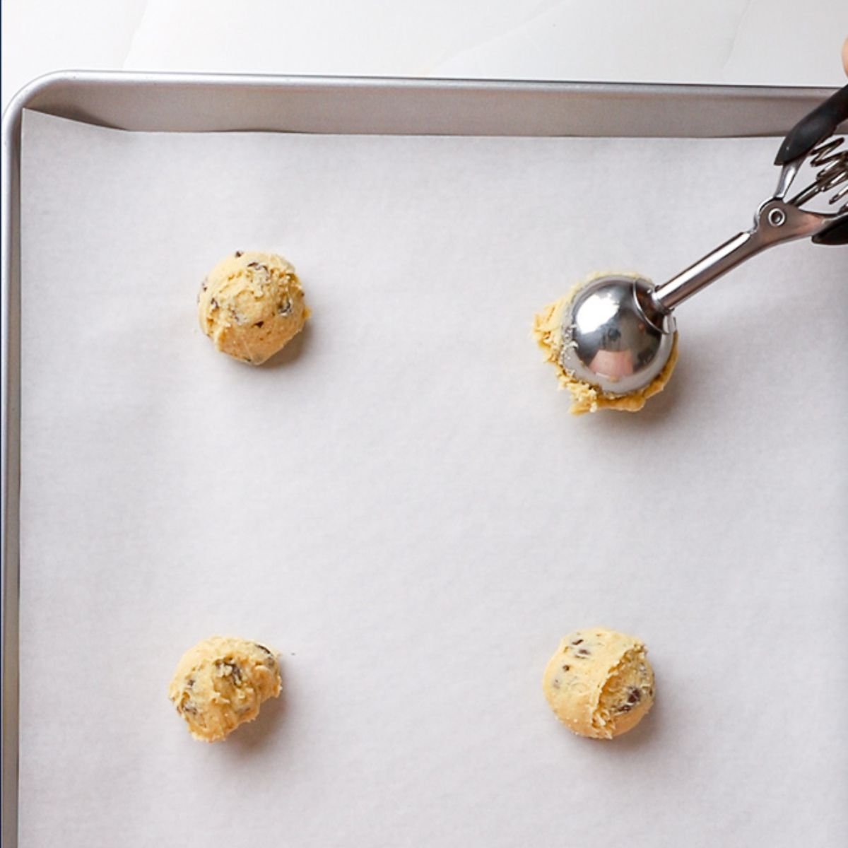 adding balls of cookie dough using an ice cream scoop to parchment lined baking sheet.