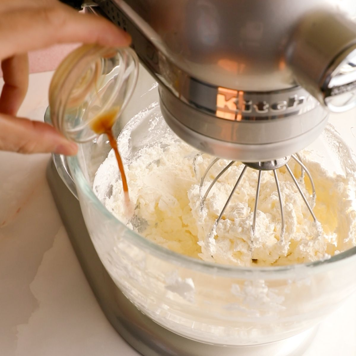 adding vanilla to a glass bowl of Italian meringue frosting.