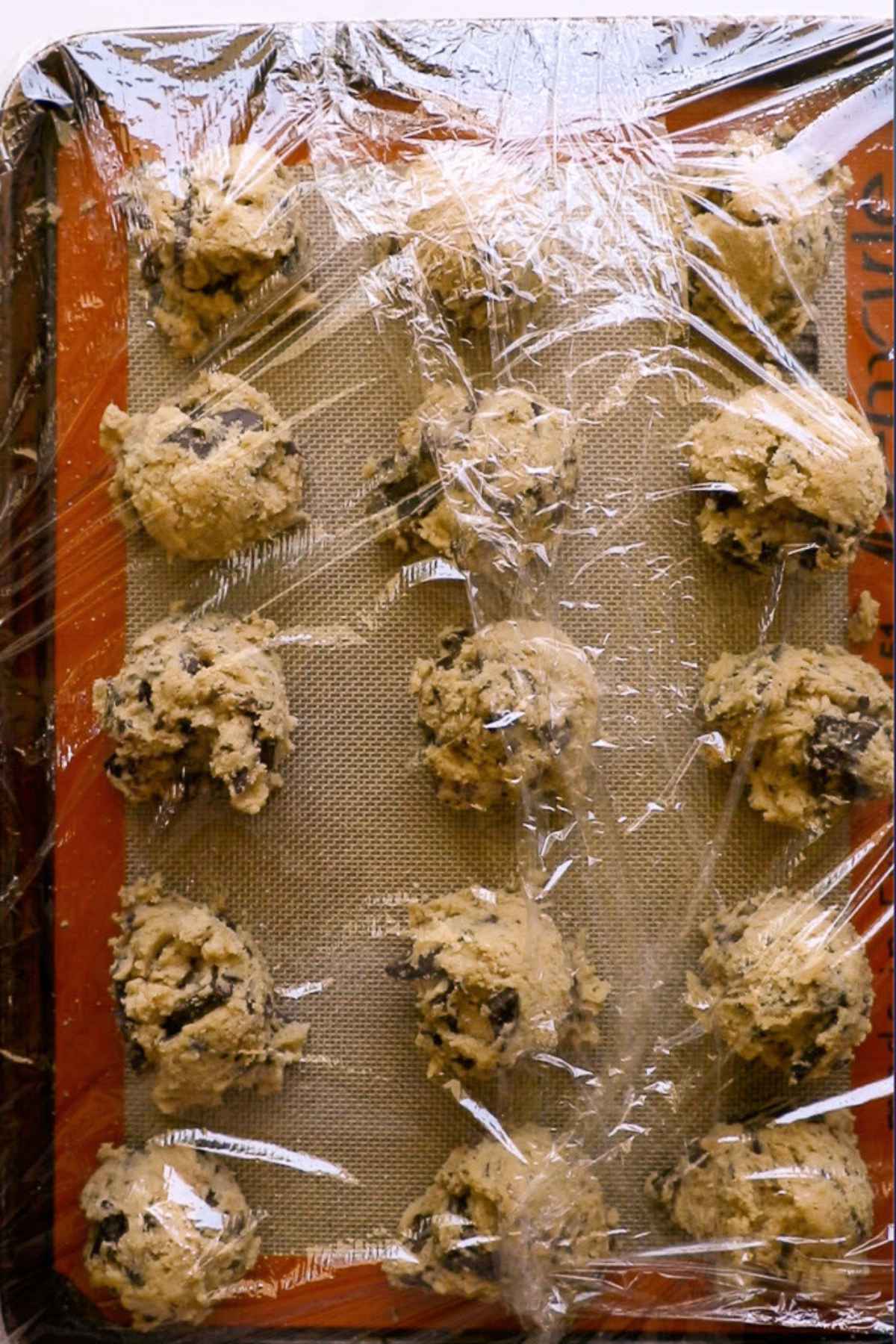 cookie dough balls on baking sheet covered in plastic wrap.