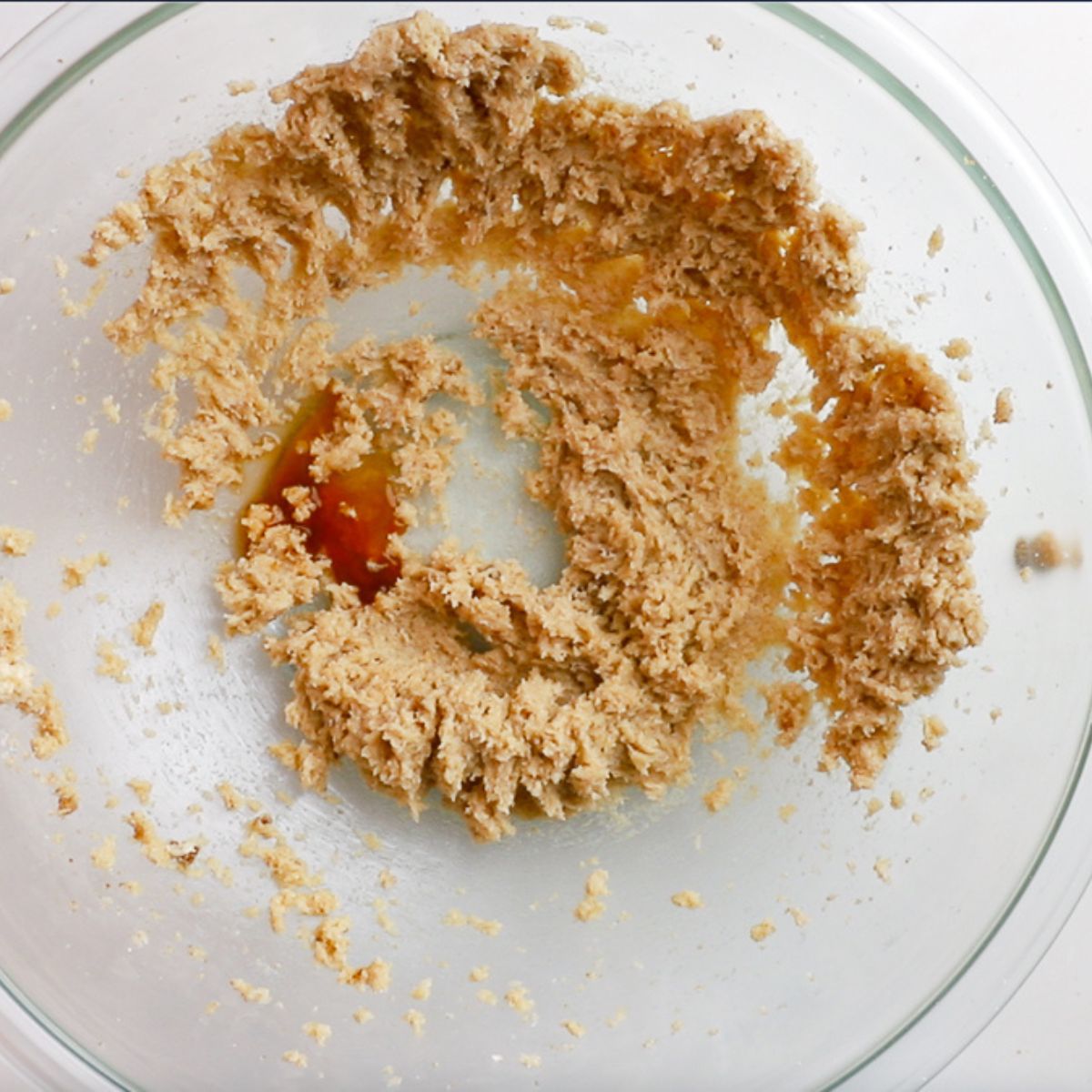 adding vanilla and water to cookie dough in glass bowl.