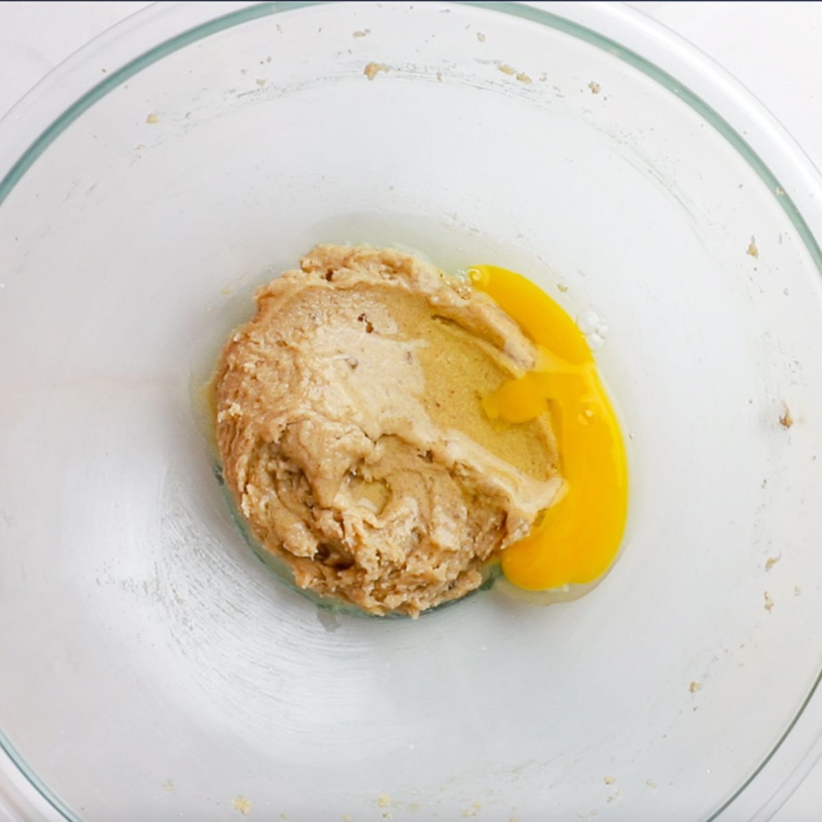 adding an egg to cookie dough in glass bowl.