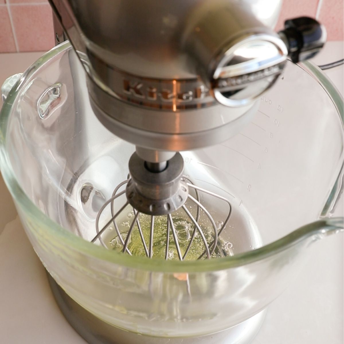 egg whites unmixed in a glass bowl of a standing mixer with a whisk attachment.